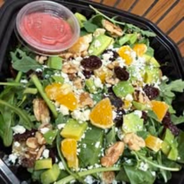 A vibrant salad with greens, avocado, oranges, nuts, and cheese, with a side of dressing.
