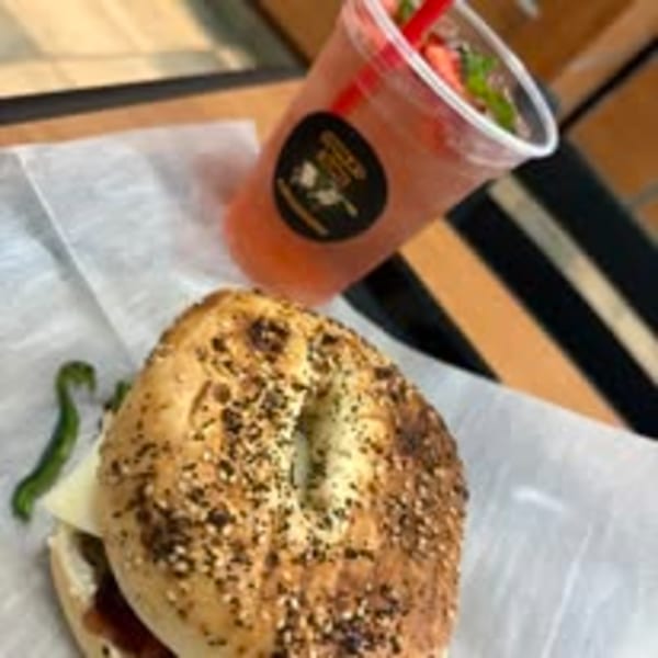 Everything bagel sandwich with cheese and green pepper, next to a pink drink with mint.