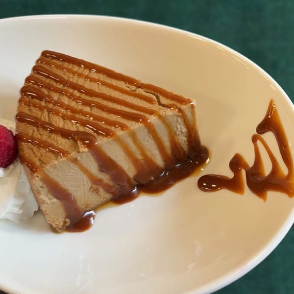 Slice of caramel cake with whipped cream and a raspberry on a white plate.