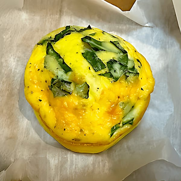 A golden-yellow egg bite with visible green spinach pieces, resting on white parchment paper.