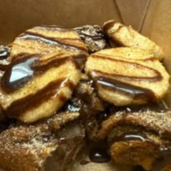 Churro bites drizzled with chocolate sauce and sprinkled with powdered sugar in a brown box.
